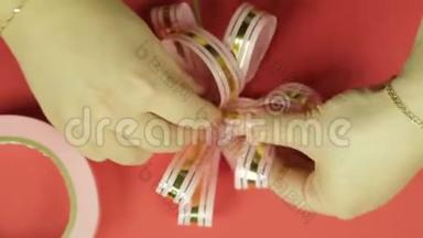 女人`双手伸直粉红色丝带礼物蝴蝶结的花瓣，给它蝴蝶结的形状。 红色背景